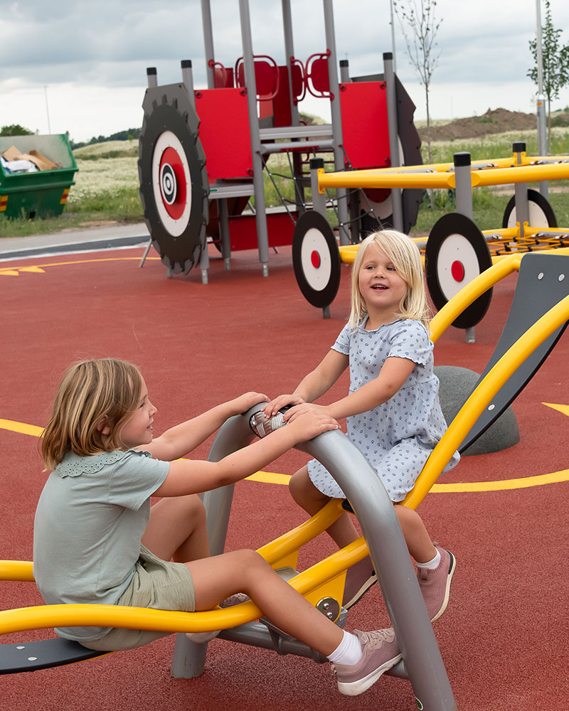 Two children play on dragonfly seesaw at a playground.